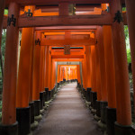 a walkway with orange pillars with Fushimi Inari-taisha in the background