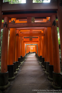 a walkway with orange pillars with Fushimi Inari-taisha in the background