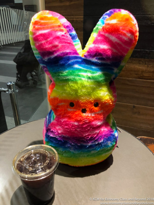 a rainbow colored stuffed bunny sitting on a table next to a drink