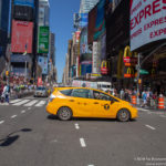 a yellow car on a street with people and buildings in the background