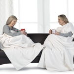 two women sitting on a couch with white blankets