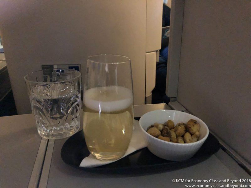 a glass of beer and a bowl of peanuts on a tray