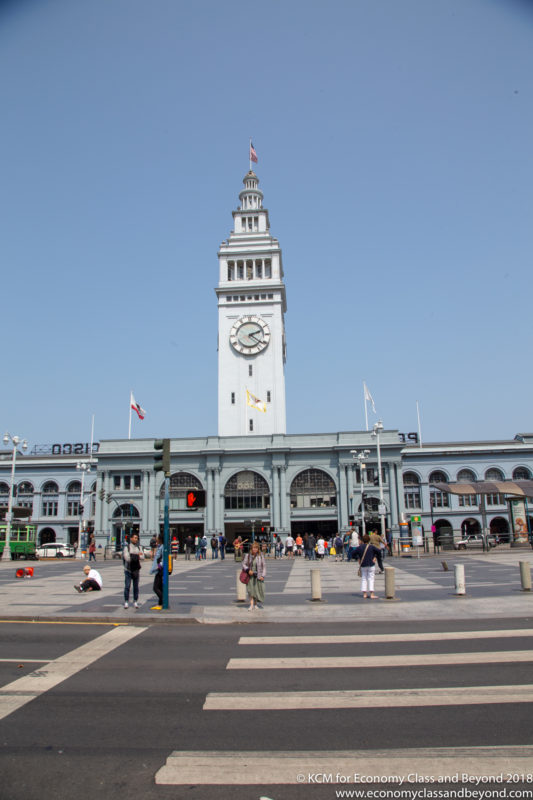 a large white tower with a clock on it with San Francisco Ferry Building in the background