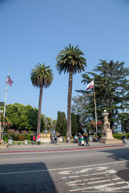 a group of people walking on a street with palm trees and flags