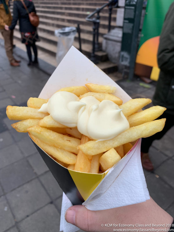 a hand holding a paper cone with french fries and mayonnaise