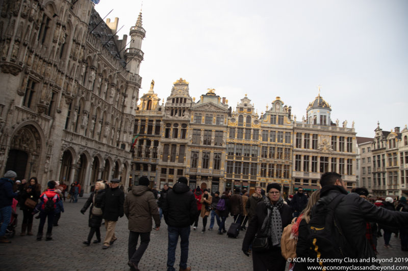 a group of people walking in a street with buildings with Grand Place in the background