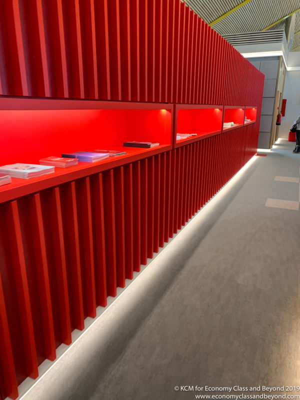 a red wall with shelves and a person walking