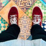 a person's legs and red shoes on a tile floor