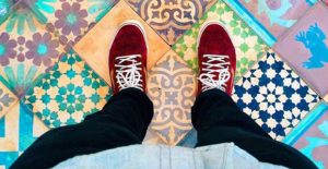 a person's legs and red shoes on a tile floor