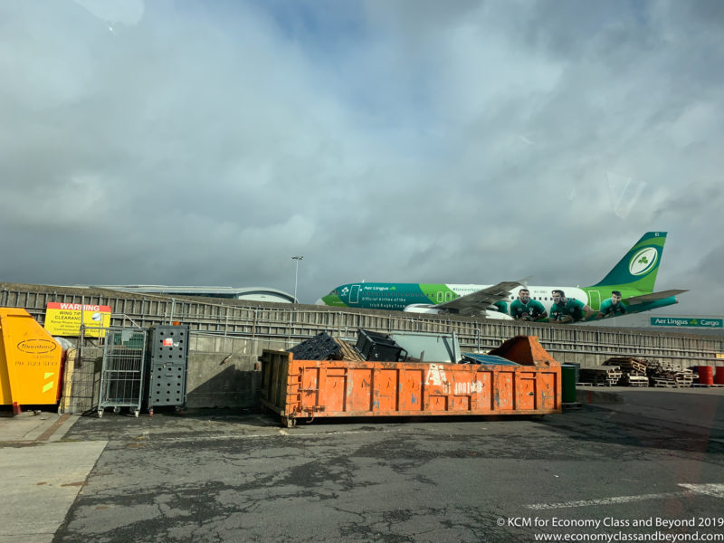 an orange dumpster next to a fence and a large green airplane