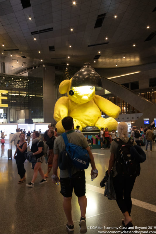 a group of people in a large building with a large yellow teddy bear