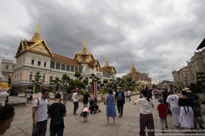 a group of people walking in front of a large building with Grand Palace in the background