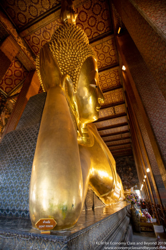 a large gold statue of a buddha with Wat Pho in the background