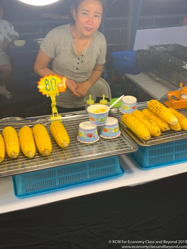 a woman standing behind a table with corn on the cob