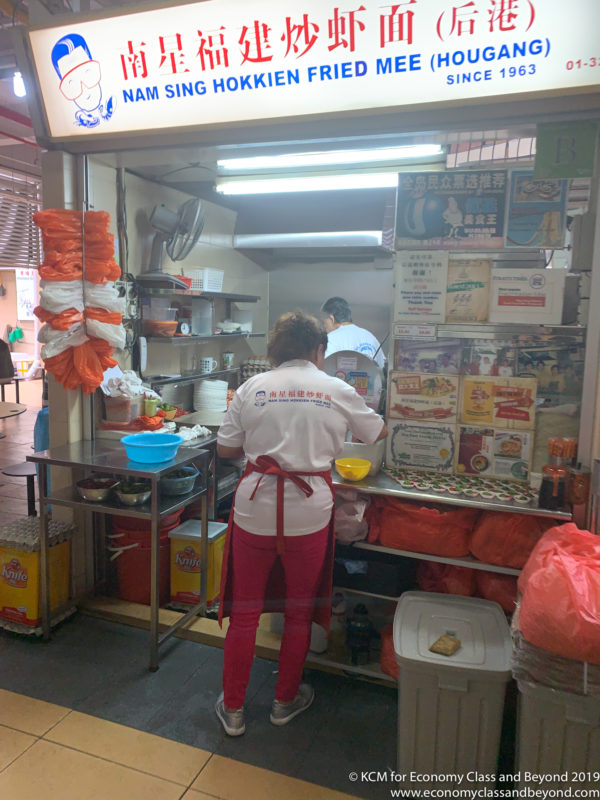 a woman in a white shirt and red pants standing in front of a food cart