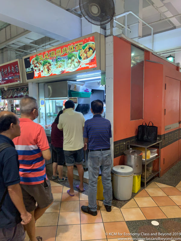 a group of people standing in a line in a food court