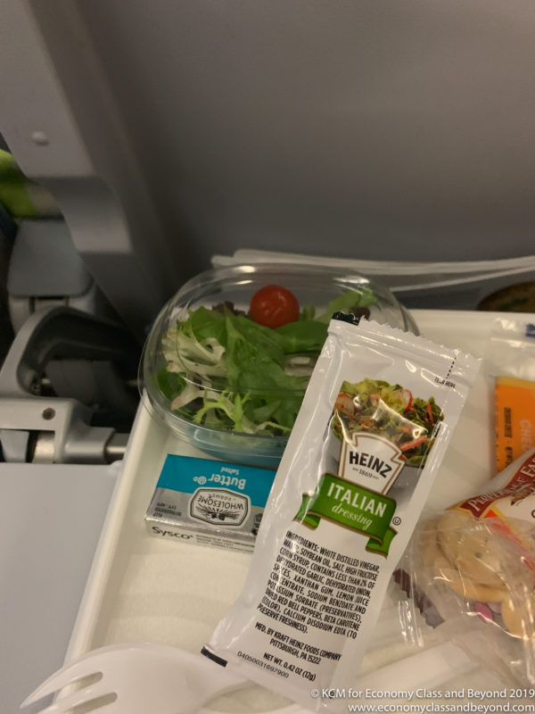 a salad and a packet of condiments on a tray