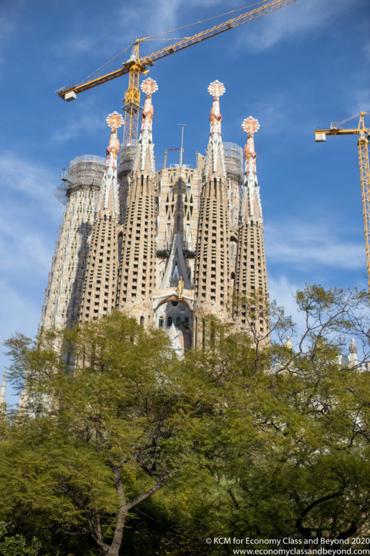 a tall building with cranes and trees with Sagrada Família in the background