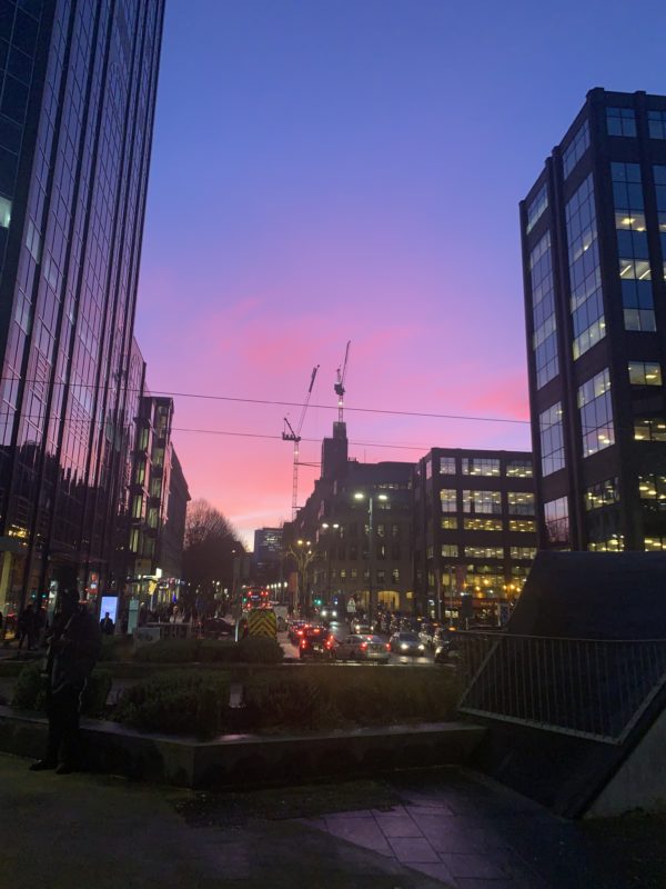 a city street with buildings and a pink and blue sky