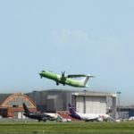 a green and white airplane flying over a runway