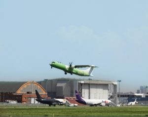 a green and white airplane flying over a runway