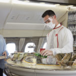 a man wearing face mask and white coat standing at a counter in an airplane