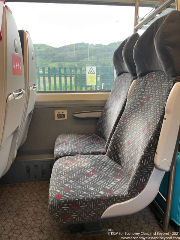 seats in a bus with a fence and mountains in the background