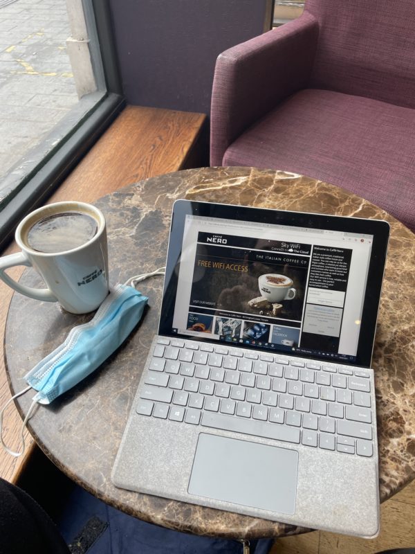 a laptop on a table with a cup of coffee and a mask