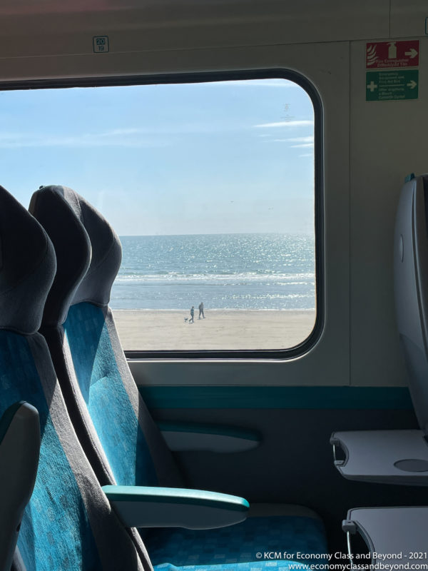 a window on a train with people walking on the beach