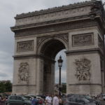 a large stone arch with statues and people in front of it with Arc de Triomphe in the background