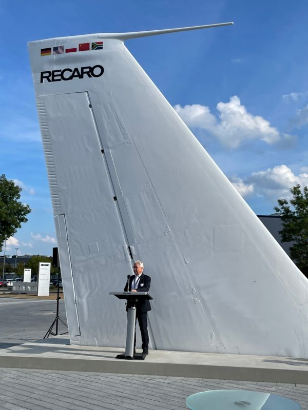 a man standing at a podium next to a tail wing