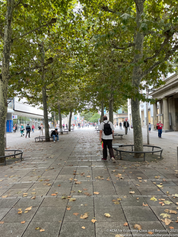 a man standing on a sidewalk with trees and people walking around