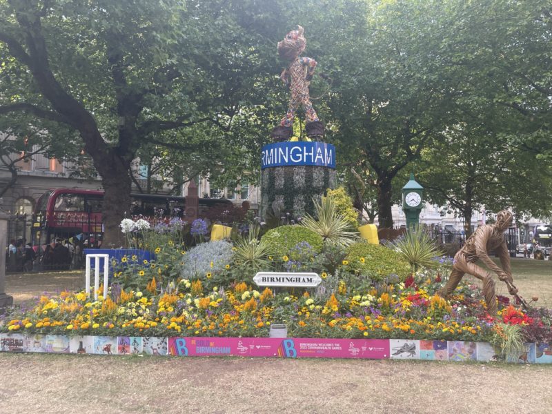 a flower garden with a statue of a man and a man in a suit