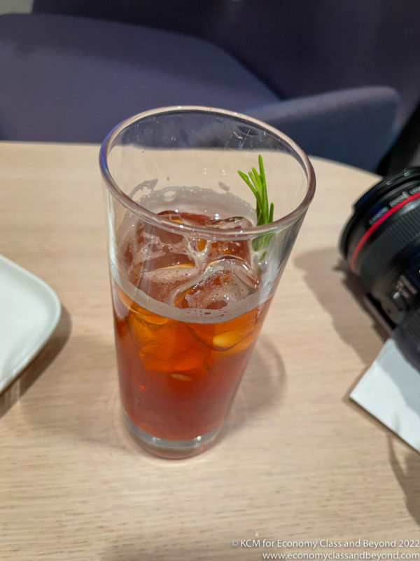 a glass of liquid with ice and a sprig of rosemary
