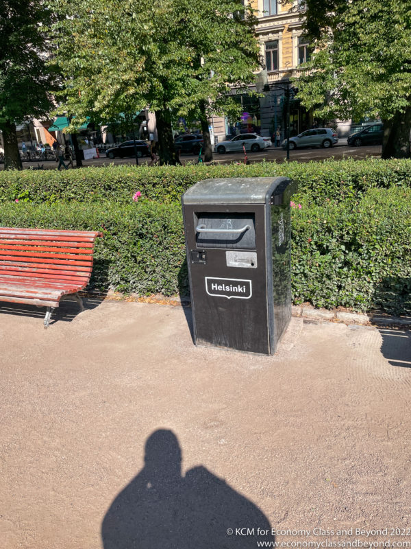 a black box on a sidewalk next to a bench