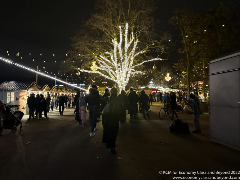 a group of people walking down a street with a tree with lights