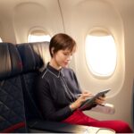 a woman sitting on an airplane with a tablet and a stylus