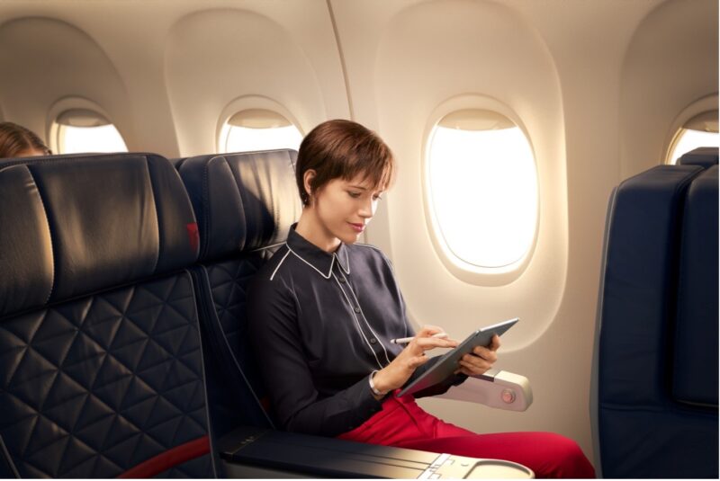 a woman sitting on an airplane with a tablet and a stylus