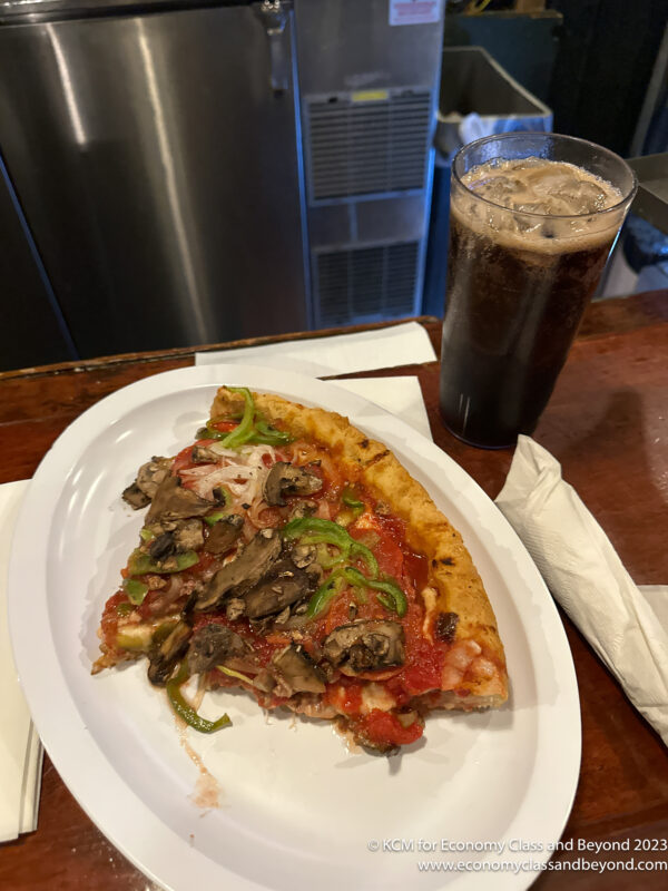 a slice of pizza on a plate next to a drink