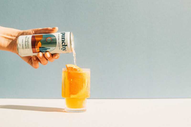 a hand pouring a can of orange juice into a glass