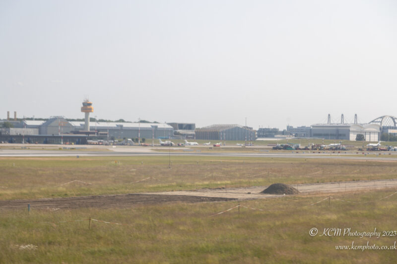 a field with a runway and buildings in the background