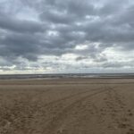 a beach with a cloudy sky with Camber Sands in the background