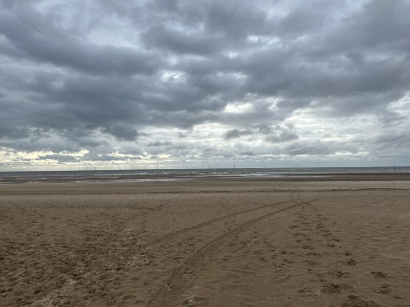a beach with a cloudy sky with Camber Sands in the background