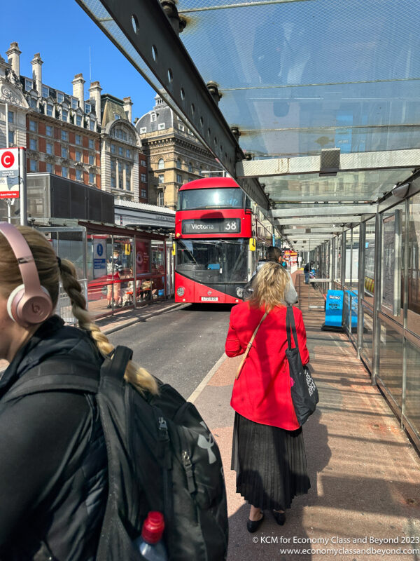 a woman standing on a bus stop with a double decker bus