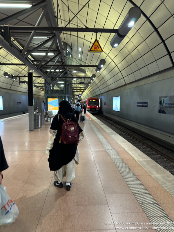 a woman in a black dress and a backpack walking on a train platform