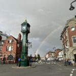 a rainbow over a street with a clock tower