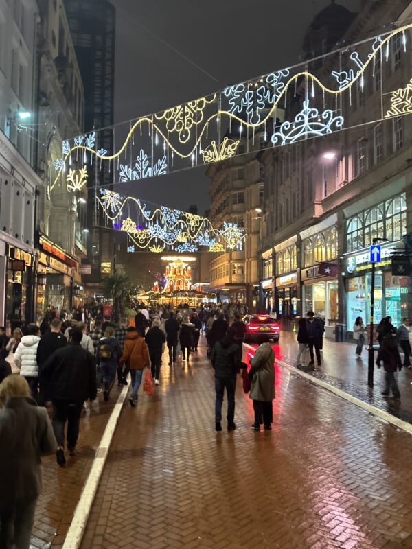a crowd of people walking down a street with lights over them