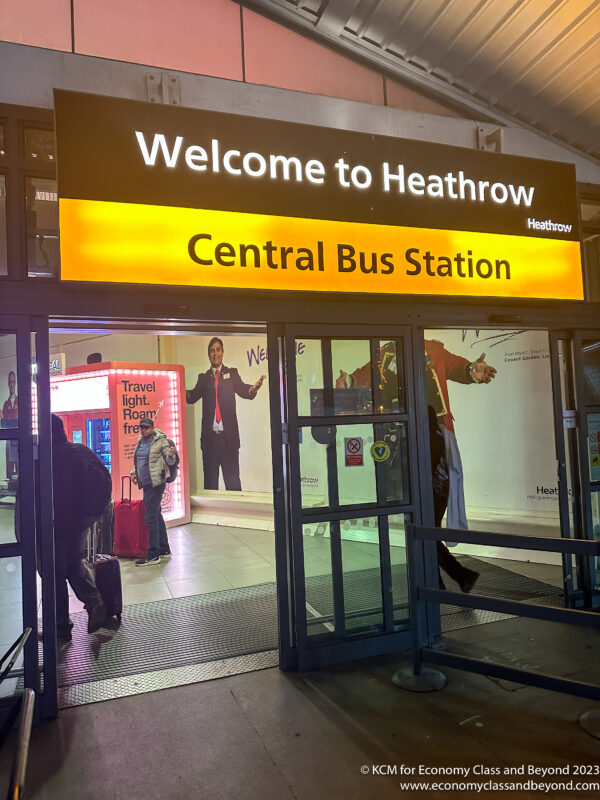 a sign with a yellow and black text and a man in a suit standing in front of a bus station