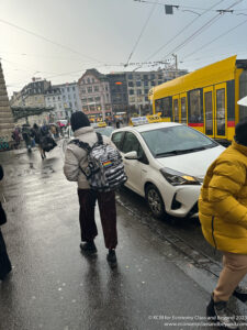 a person with a backpack walking on a street with a car and a bus