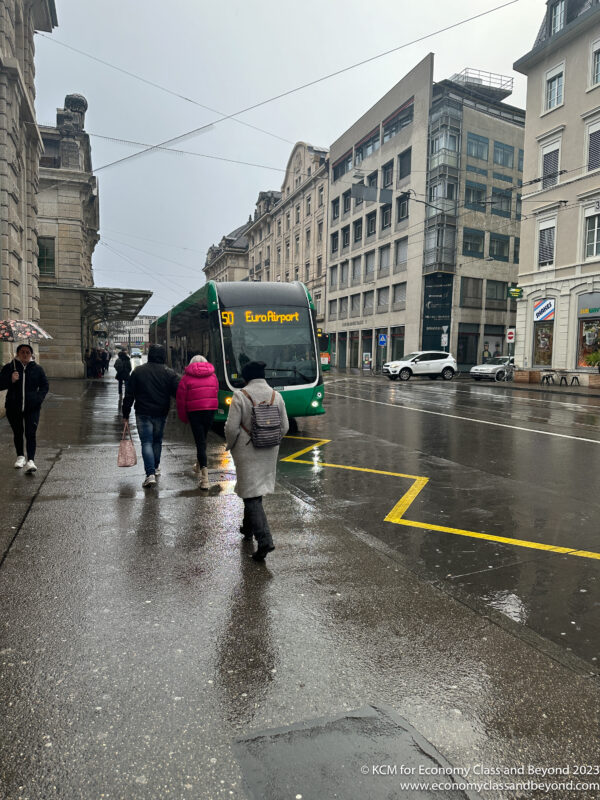 people walking on a wet street with a bus and people walking